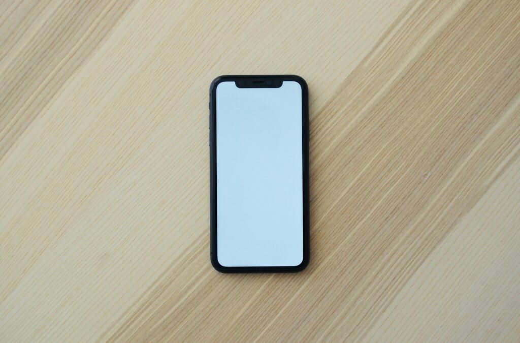 A black smartphone with a blank white screen on a light wooden surface